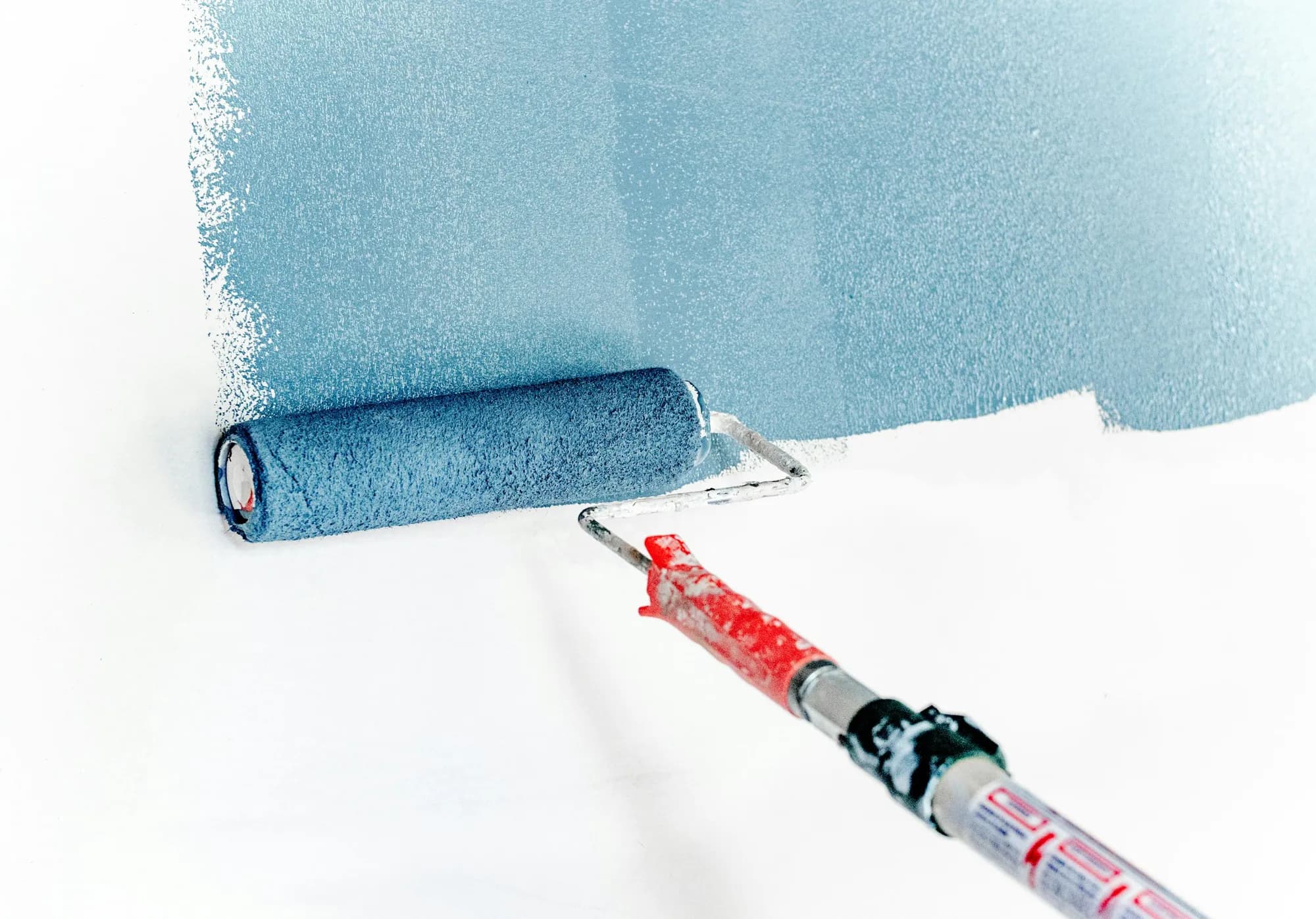 Stock photograph of a paint roller applying blue paint to a white wall